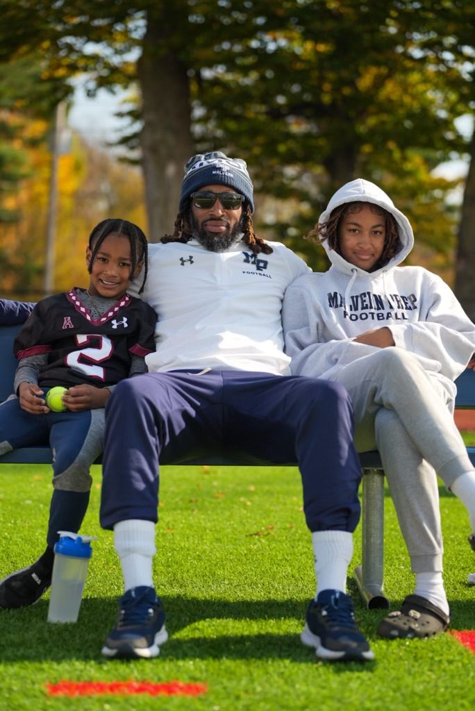 Coach Dante Coles sitting on a bench outdoors with two of his children