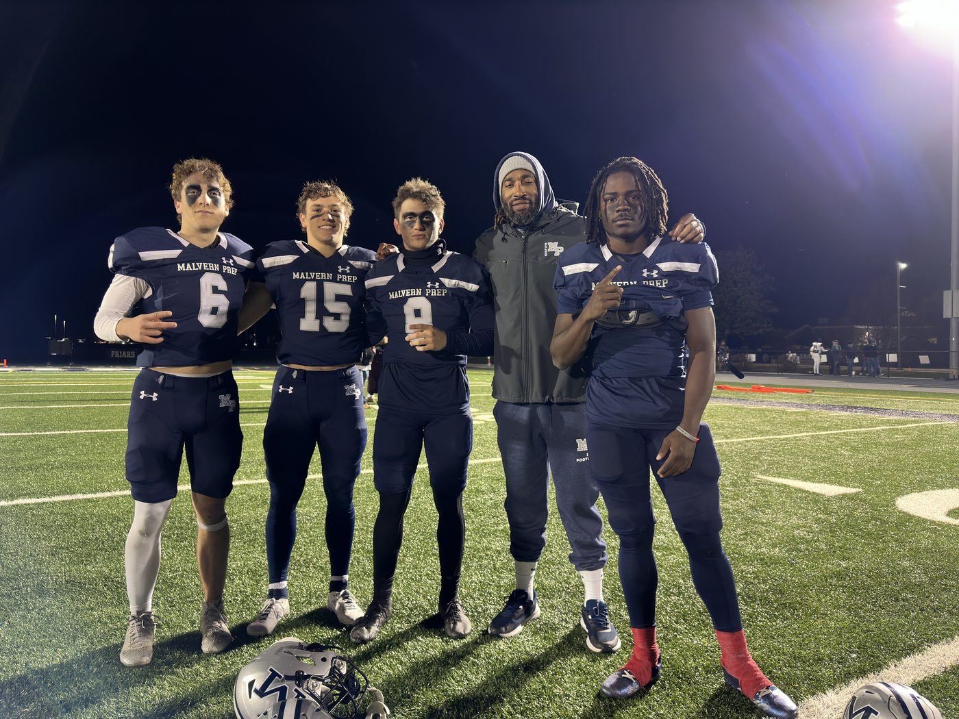 Coach Dante Coles posing on the field at night with four of his players in uniform