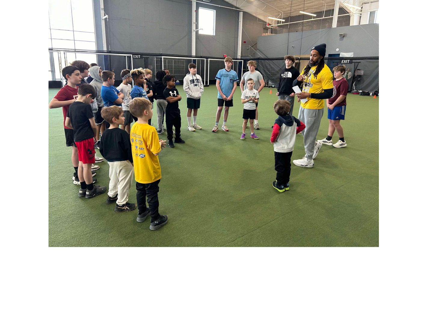 Coach Dante Coles talking with a huddle of young athletes during an indoor training session